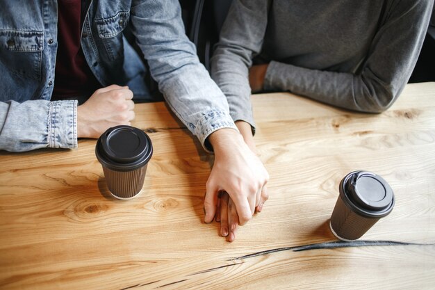 Couple d'étudiants ayant un déjeuner romantique à l'intérieur se tenant la main clo