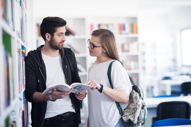 Un couple d'étudiants heureux dans la bibliothèque de l'école discutent d'un livre.