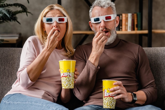 Couple excité dans des lunettes 3d mangeant du pop-corn et regardant un film sur un canapé