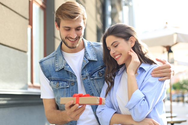 Couple excité étonné en vêtements d'été souriant et tenant la boîte présente ensemble tout en se tenant dans la rue de la ville.