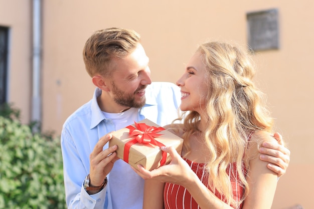 Couple excité étonné en vêtements d'été souriant et tenant la boîte présente ensemble tout en se tenant dans la rue de la ville.