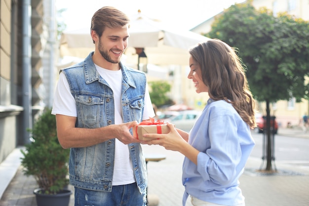 Couple excité étonné en vêtements d'été souriant et tenant la boîte présente ensemble tout en se tenant dans la rue de la ville.