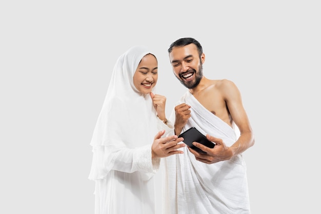 Couple excité portant des vêtements ihram regardant une vidéo à l'aide d'un smartphone