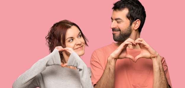 Couple faisant le symbole du coeur à la main sur fond rose isolé