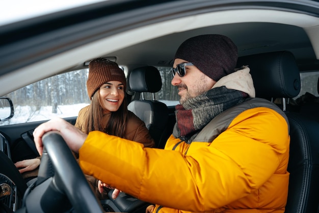 Couple de famille assis dans la voiture en vêtements d'hiver dans la forêt de neige