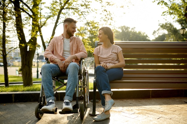 Couple avec fauteuil roulant assis sur un banc dans le parc