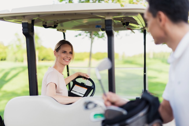 Couple femme conduit une voiture de golf sur le parcours de golf.