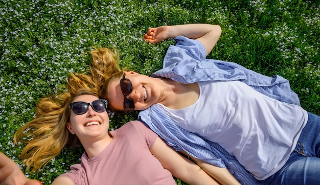 Couple de femmes aimantes allongé face à face sur le pré en fleurs, sérénité, jeunesse, amour unisexe, amitié