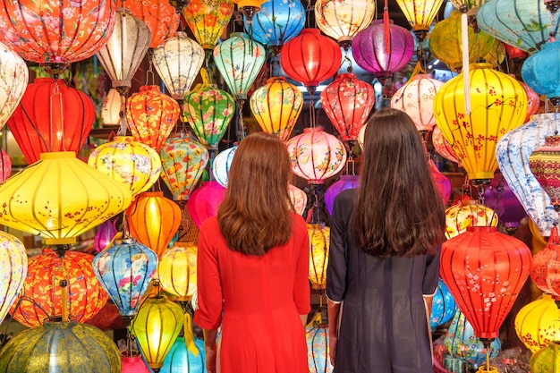 Couple de femmes portant une robe vietnamienne Ao Dai avec une lanterne colorée voyageur visitant Hoi An ville ancienne dans le centre du Vietnampoint de repère pour les attractions touristiquesVietnam et concept de voyage du sud-est