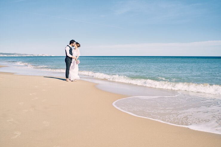 Photo couple fiancé s'embrassant sur la plage en robes de mariée
