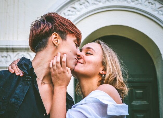 Couple de filles debout s'embrassant dans une porte vert foncé dans la rue