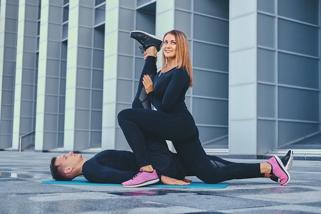 Le couple de fitness athlétique s'exerce sur un tapis aérobie sur fond de bâtiment moderne.