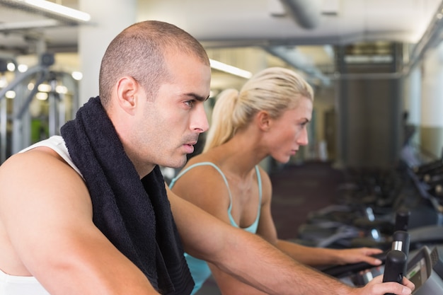 Couple en forme déterminé travaillant sur des vélos d&#39;exercice au gymnase