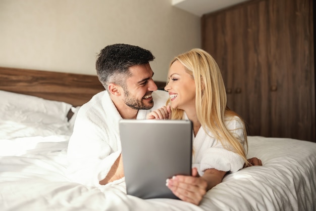 Couple fraîchement marié s'embrassant et tendre dans un lit confortable avec des draps blancs