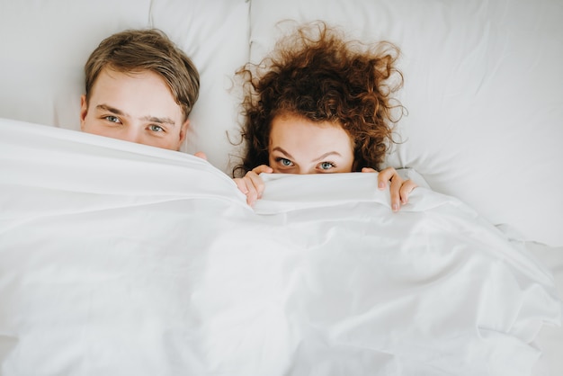 Photo couple fuuny se cachant sous une couverture blanche