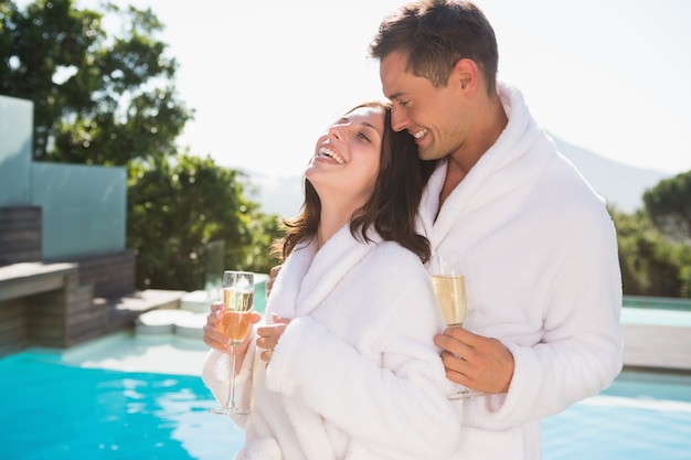 Couple gai avec des flûtes à champagne au bord de la piscine