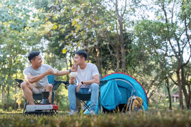 Un couple gay asiatique voyageant avec une tente camping en plein air et diverses aventures style de vie randonnée vacances d'été actives boire du café et parler ensemble.