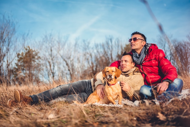 Couple gay couché sur une couverture en herbe avec chien