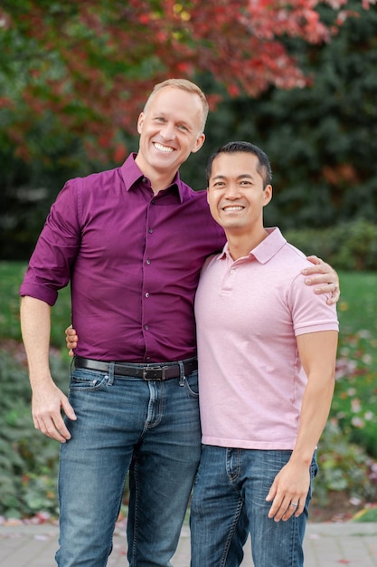 couple gay souriant deux hommes s'embrassant regardant la caméra posant debout dans un parc sur une rue urbaine Lgbt