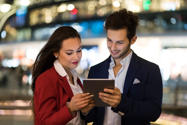 Couple de gens d&#39;affaires à l&#39;aide d&#39;une tablette en plein air la nuit dans un cadre de la ville moderne