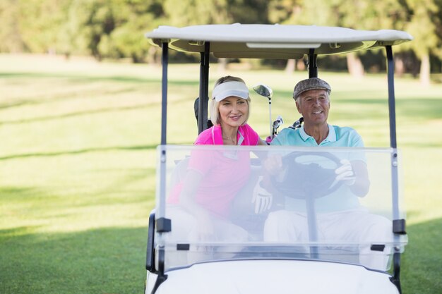 Couple de golfeurs matures assis dans un buggy de golf