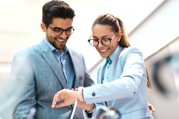 Couple habillé en costume vérifiant la nouvelle montre-bracelet. Femme portant une montre, regardant et essayant. Intérieur du magasin Tech.