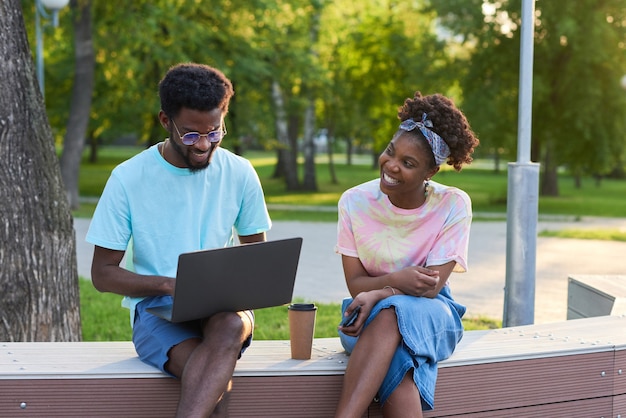 Couple heureux africain utilisant un ordinateur portable et travaillant en ligne ensemble tout en étant assis dans le parc