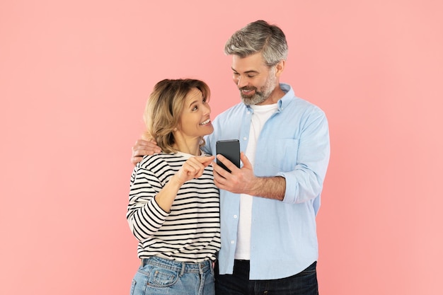 Couple heureux à l'aide de femme smartphone pointant sur fond rose de téléphone