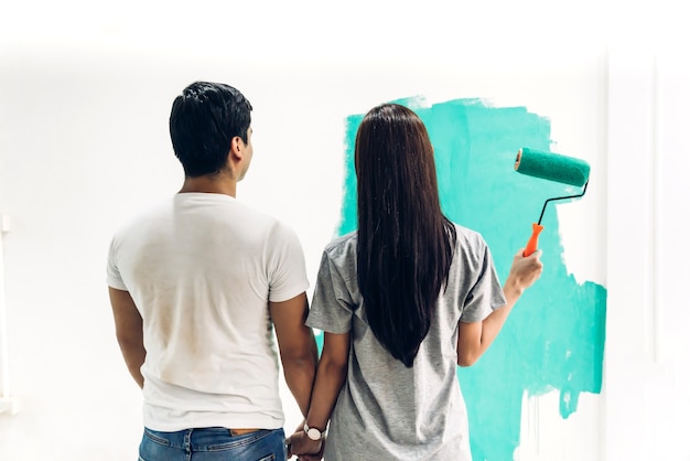 Couple Heureux à L'aide D'un Rouleau à Peinture Et De La Peinture Des Murs Dans Leur Nouvelle Maison