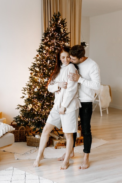 couple heureux amoureux dans un salon confortable blanc avec des décorations de Noël et un arbre de Noël