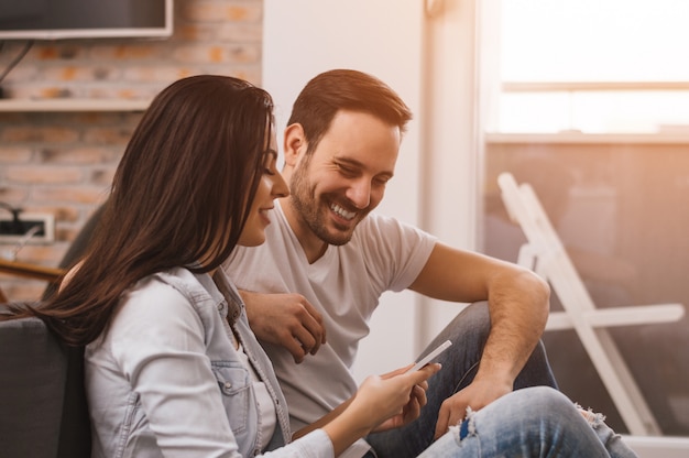 Couple heureux, appréciant le contenu multimédia dans un téléphone intelligent, assis sur le sol