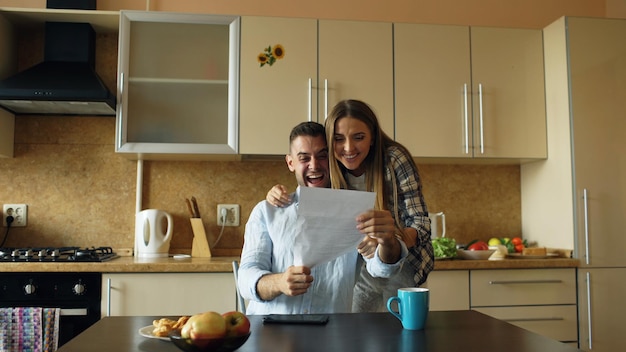Un couple heureux et attrayant reçoit une bonne nouvelle qui dévoile une lettre dans la cuisine tout en prenant son petit-déjeuner