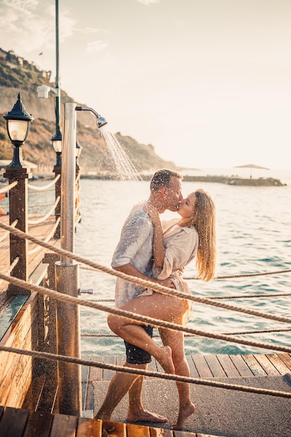 Couple heureux au bord de la mer Un gars et une fille sont sous la douche sur une jetée en plein air Couple heureux en vacances Homme et femme au bord de la mer