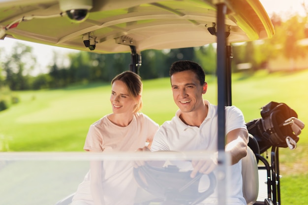 Couple heureux au volant d&#39;une voiture de golf transportant des bâtons de golf.