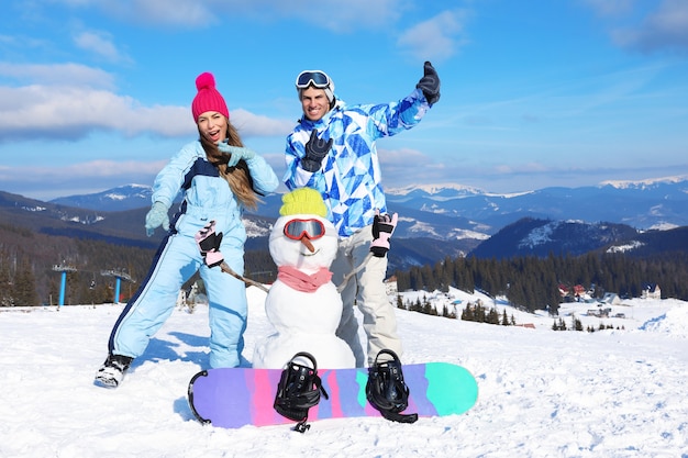 Couple heureux avec bonhomme de neige s'amusant à la station de ski. Vacances d'hiver