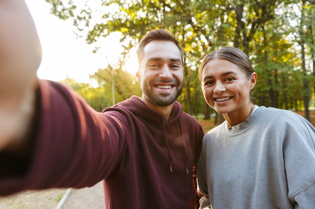 couple heureux caucasien en tenue de sport prenant une photo de selfie et signe souriant dans un parc verdoyant