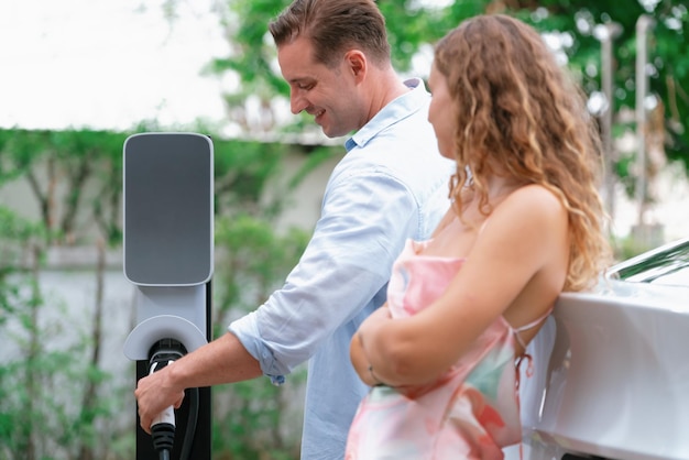 Couple heureux et charmant avec un véhicule électrique de recharge respectueux de l'environnement à partir de la station de recharge EV La technologie des voitures EV est utilisée comme moyen de transport alternatif pour la durabilité future Synchronos