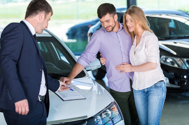 Couple heureux avec un concessionnaire automobile dans un salon de l'auto ou un salon