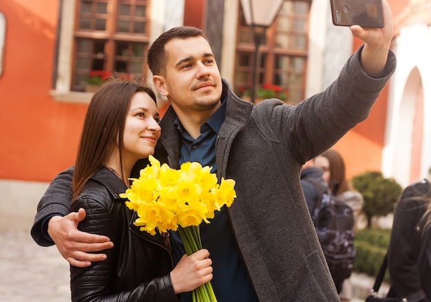 Couple heureux avec des fleurs faisant selfie dans la rue.