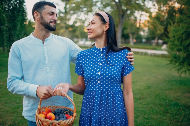 Couple heureux avec des fruits dans un panier pique-nique séjournant dans le parc.