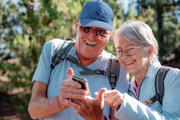 Un couple heureux d'hommes et de femmes retraités en randonnée dans un parc de montagne s'arrête pour regarder un téléphone portable