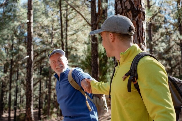 Couple heureux et insouciant de grand-père et petit-fils adolescent en randonnée dans les montagnes partageant la même passion pour la nature et un mode de vie sain ensemble dans les bois