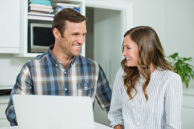 Couple heureux interagissant les uns avec les autres tout en utilisant un ordinateur portable dans le salon