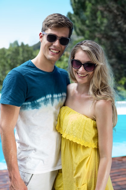 Couple heureux en lunettes de soleil debout près de la piscine
