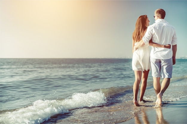 Couple heureux marchant sur la plage au bord de la mer