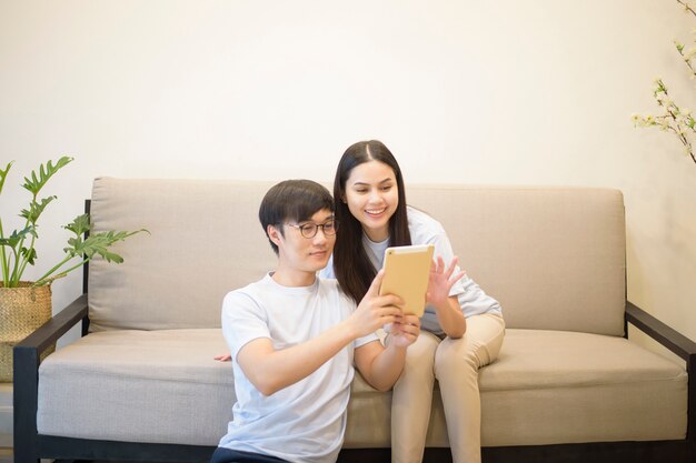 Un couple heureux portant une chemise bleue se détend et tient une tablette sur un canapé à la maison