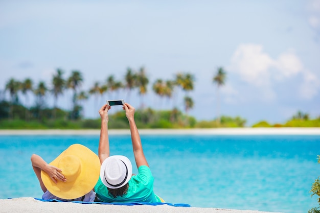 Couple heureux prenant une photo sur la plage blanche en vacances de lune de miel