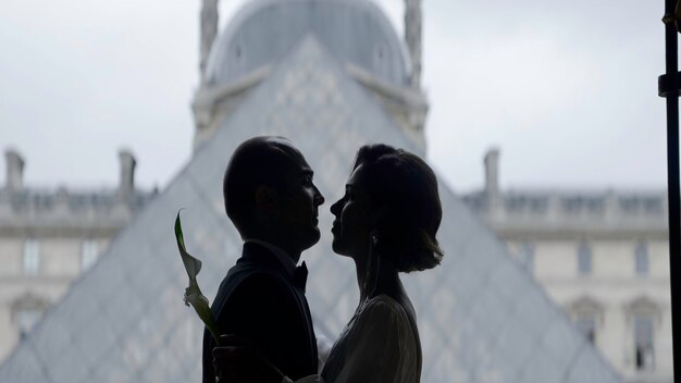 Photo couple heureux près de la pyramide du musée du louvre à paris. vue latérale de la mariée et du marié s'embrassant.