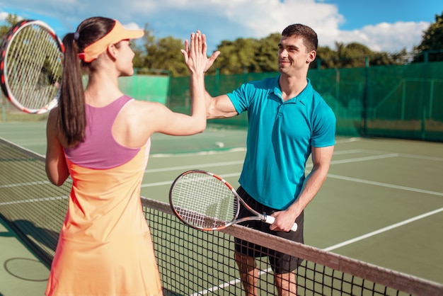Couple heureux avec des raquettes jouant sur un court de tennis extérieur.