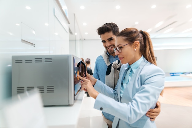 Couple heureux à la recherche de nouveaux micro-ondes à acheter en se tenant debout dans le magasin tech